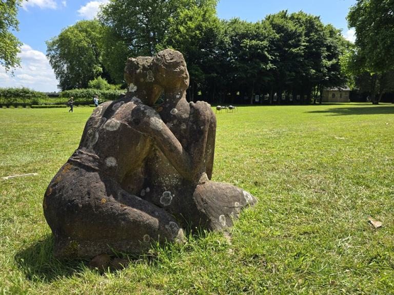 Das Bild zeigt zwei Skulpturen von Frauen, die auf einer Wiese hocken