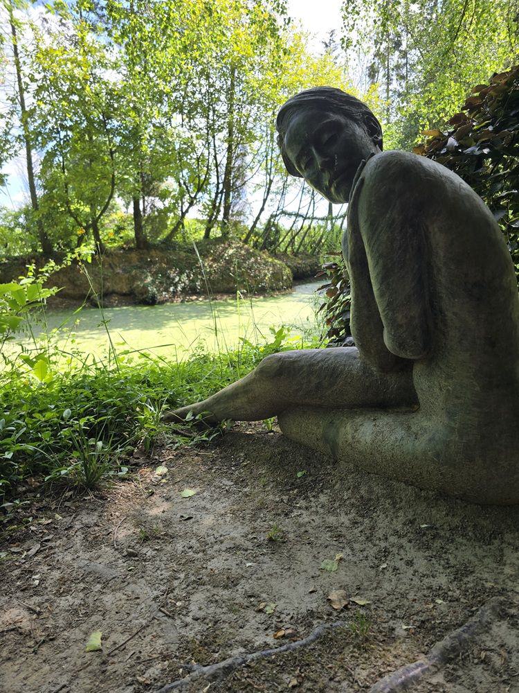 Skulptur einer sitzenden Frau vor einem Teich