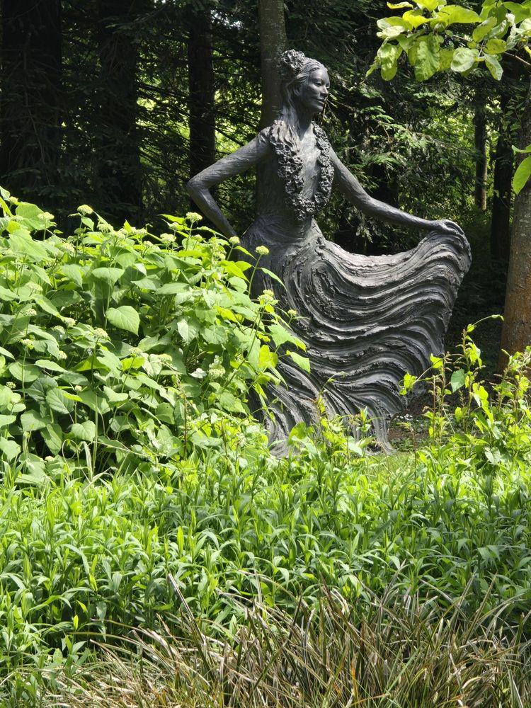 Das Bild zeigt eine Frauenskulptur mit einem weiten Rock, der von der Frau mit einer Hand angehoben wird.