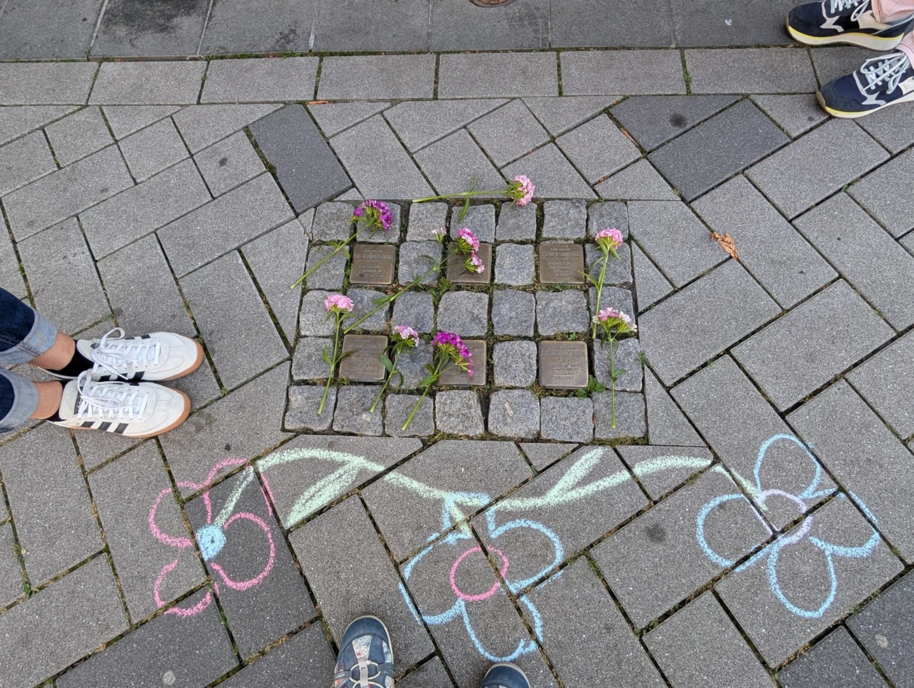6 Stolpersteine die mit Kreidezeichnungen umrankt sind und auf denen Blumen abgelegt sind.